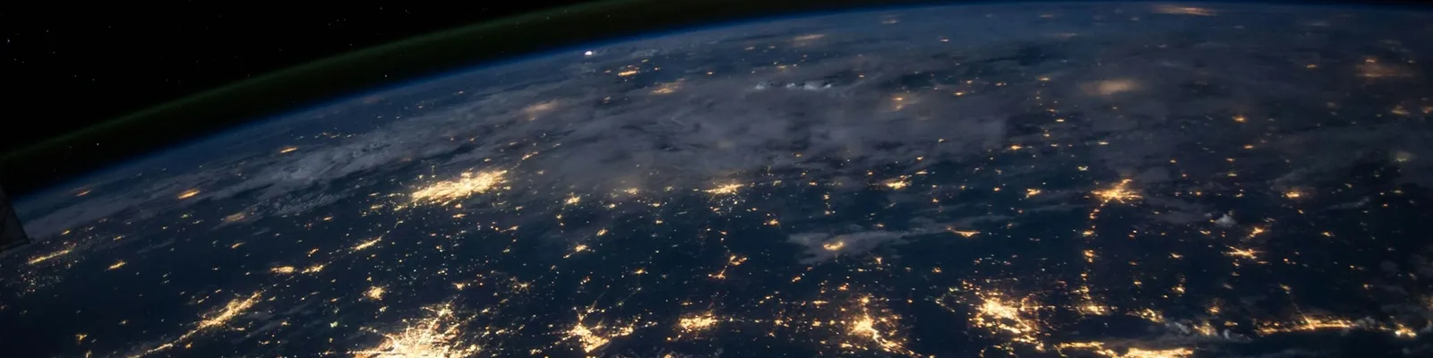View of Earth from space at night, showing illuminated cities and networks across continents under a starry sky.